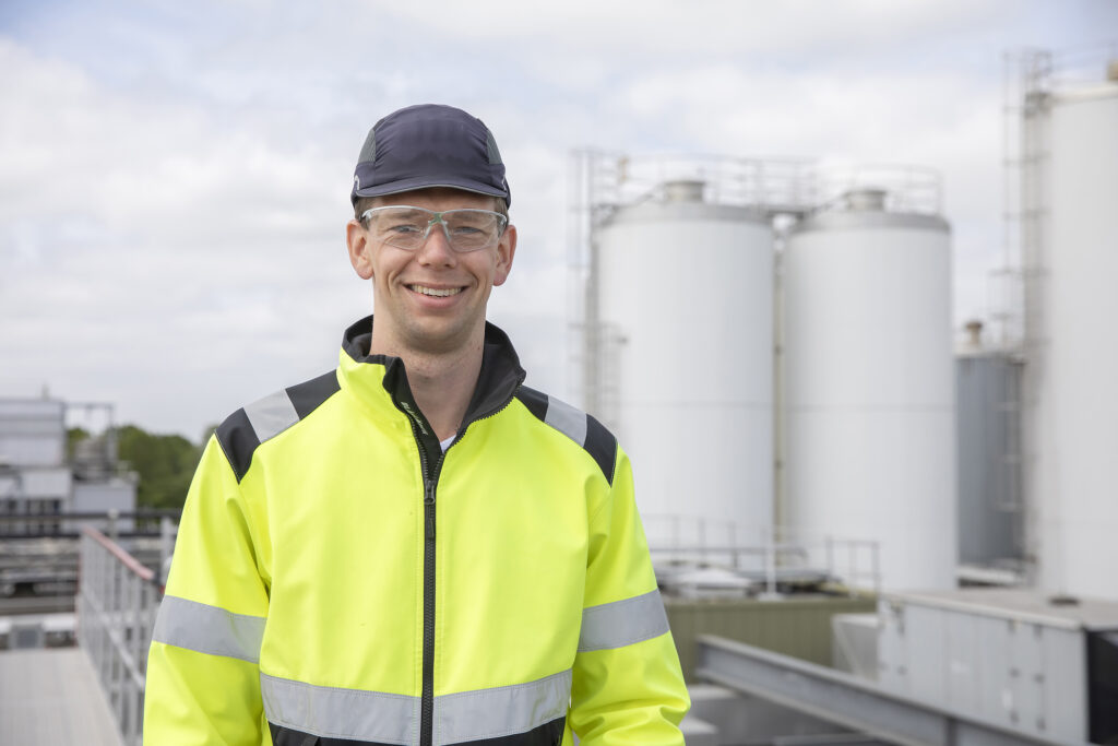 Jasper Faber, project manager at FrieslandCampina Gerkesklooster, wearing a safety jacket and glasses, standing in front of the industrial plant.