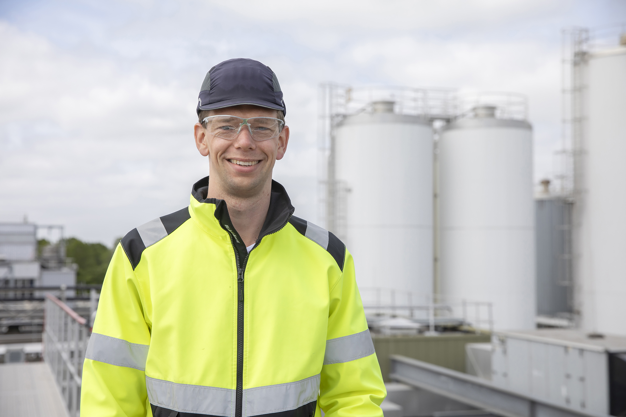 Jasper Faber, project manager at FrieslandCampina Gerkesklooster, wearing a safety jacket and glasses, standing in front of the industrial plant.