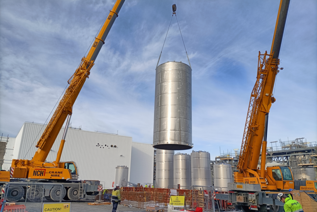 Installing a large stainless steel storage tank on site with cranes