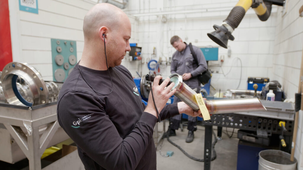 Foreman Rob Jansen inspecting a stainless steel nozzle assembly in the welding pre-production workshop at Gpi Tanks, with a colleague working in the background.